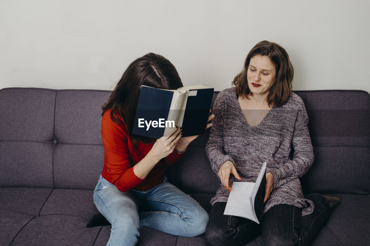 Young females holding book sitting on sofa at home