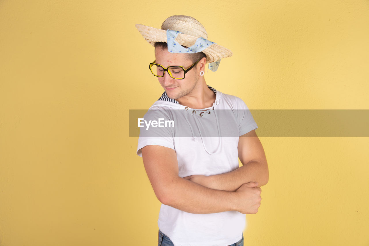 Smiling young man with arms crossed standing against yellow background