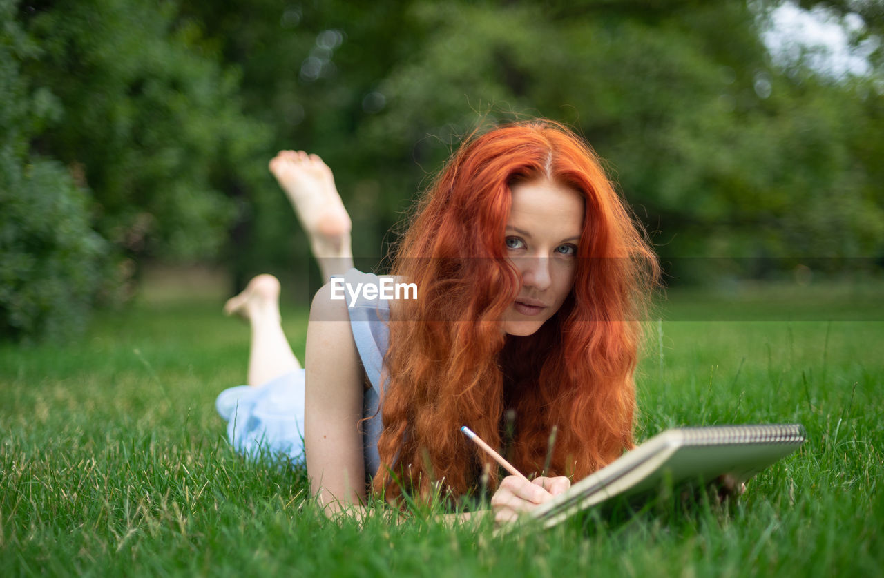 Portrait of redhead woman with book lying on grass