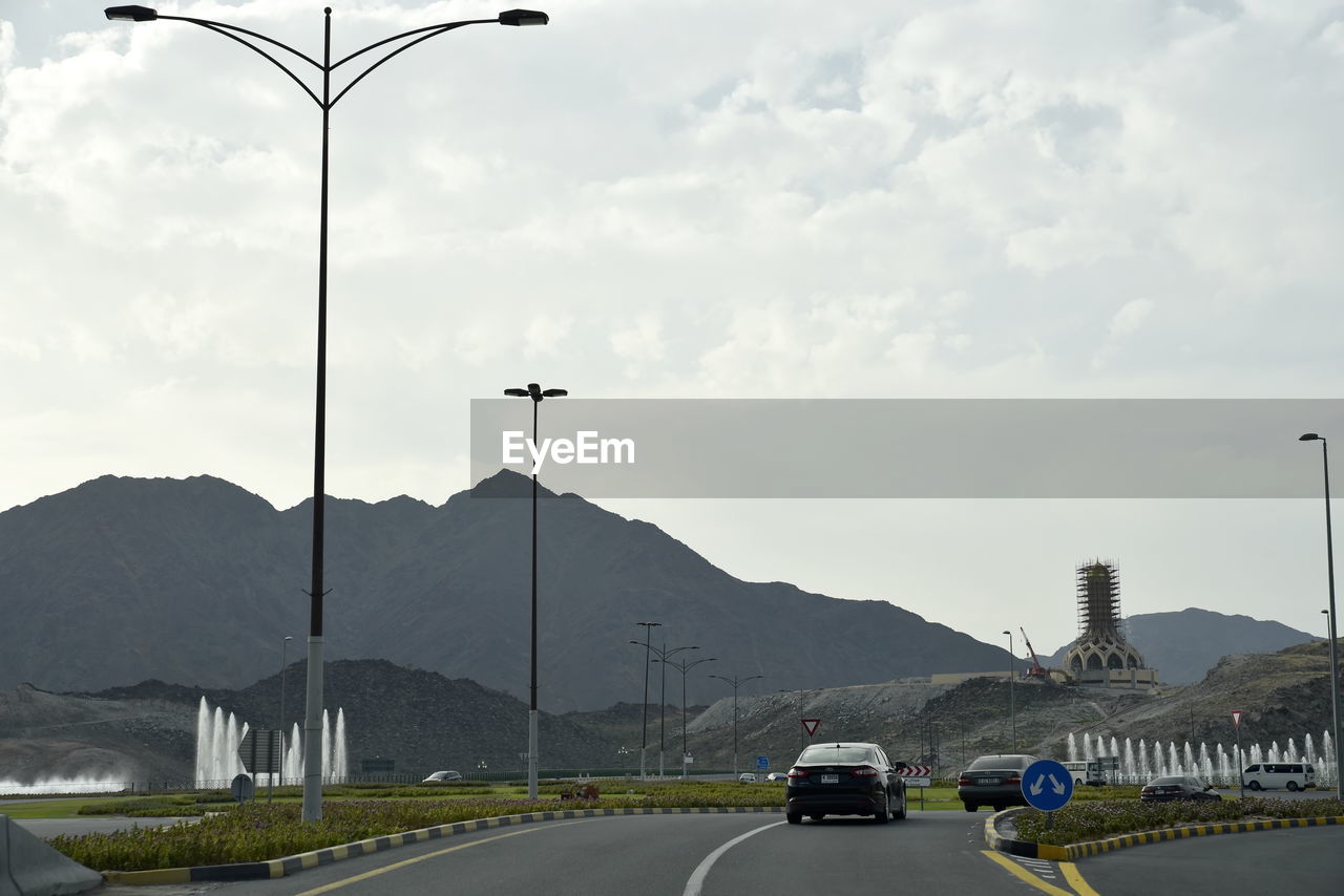 CARS ON ROAD AGAINST MOUNTAIN RANGE