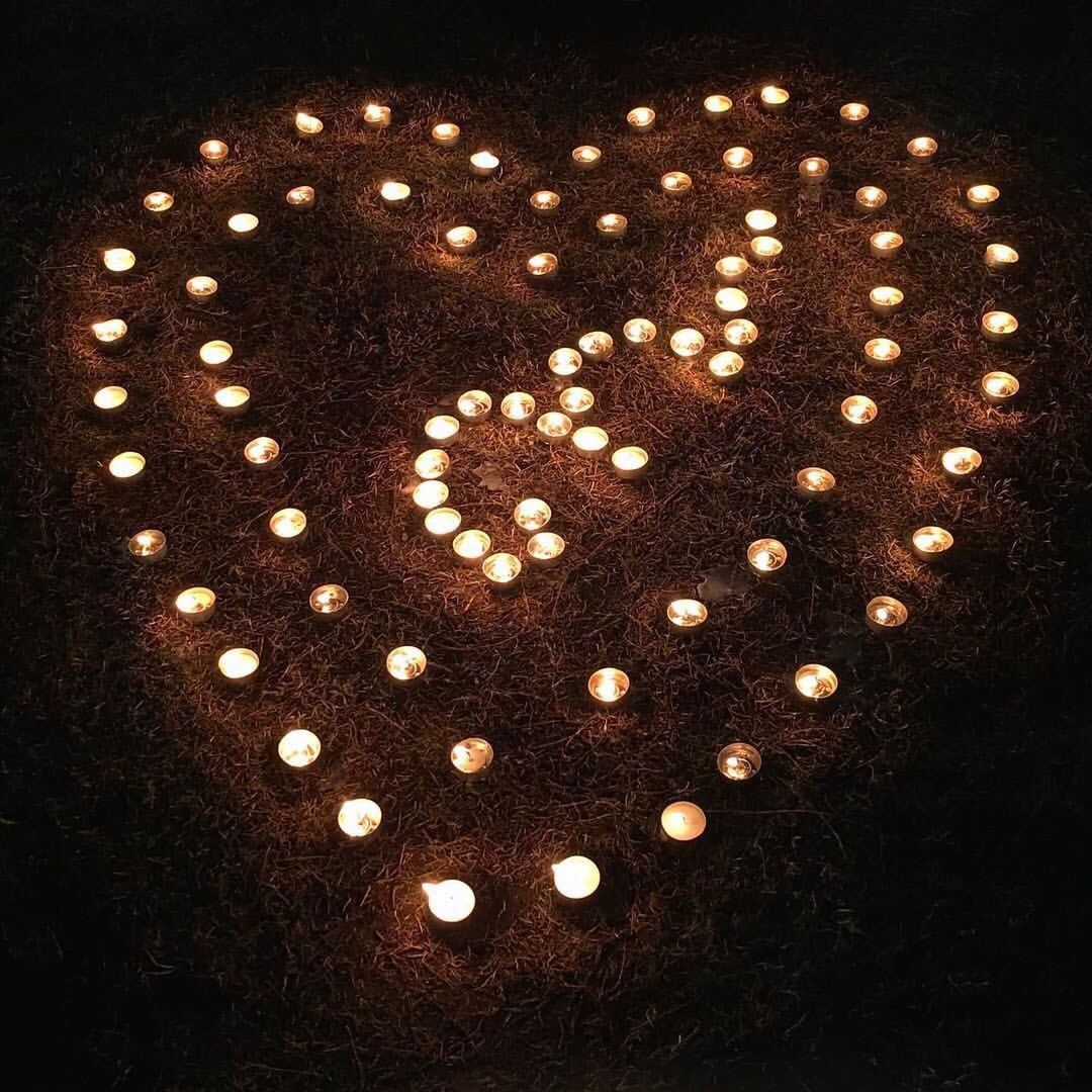 High angle view of lit tea lights candles arranged heart shaped on field
