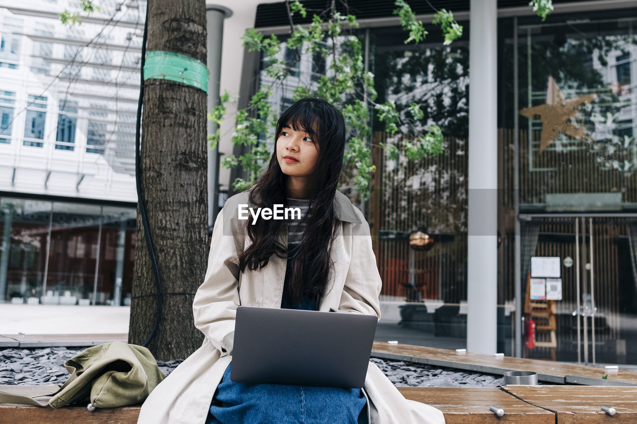 Young woman with laptop sitting in front of building