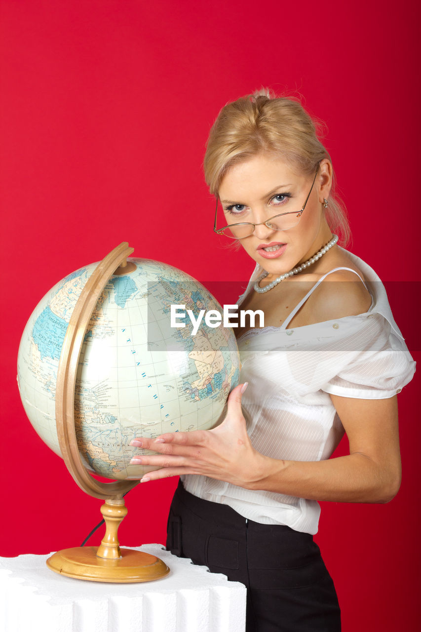 Portrait of businesswoman standing by globe against red background