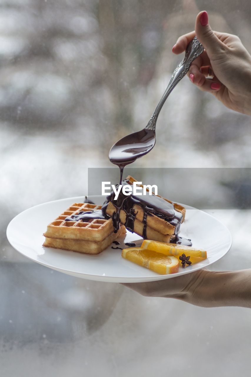 Cropped hand of person pouring chocolate on food