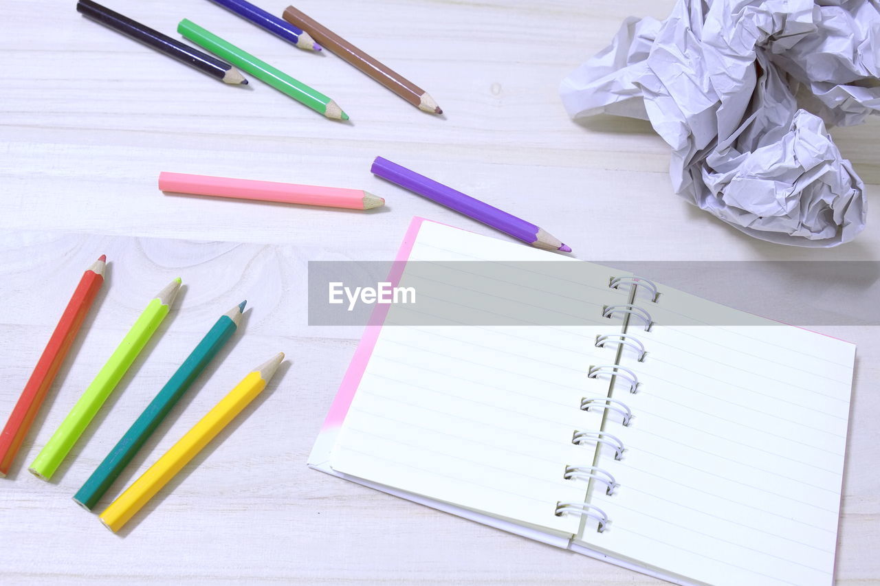 High angle view of colored pencils with diary on table