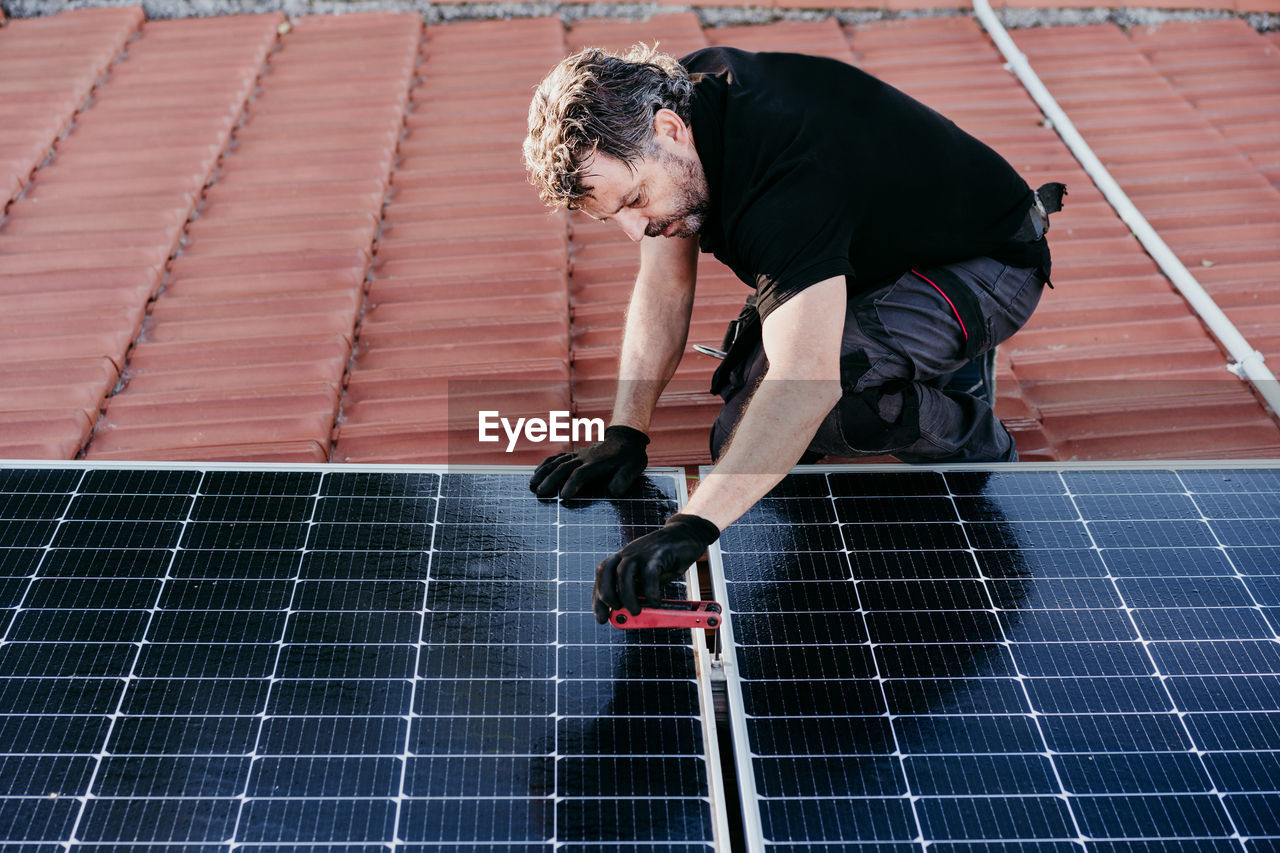 Mature technician man assembling solar panels on house roof for self consumption. renewable energies