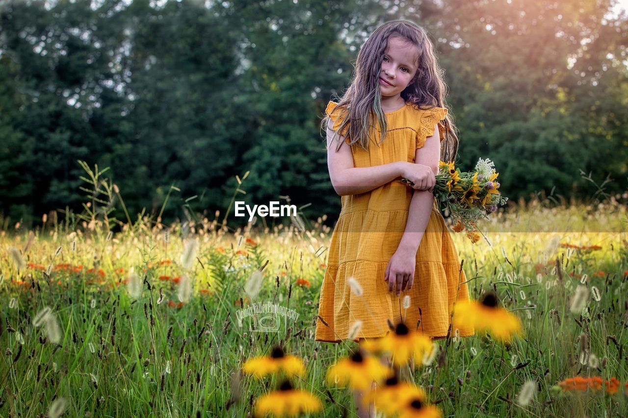 full length of young woman standing amidst plants on field