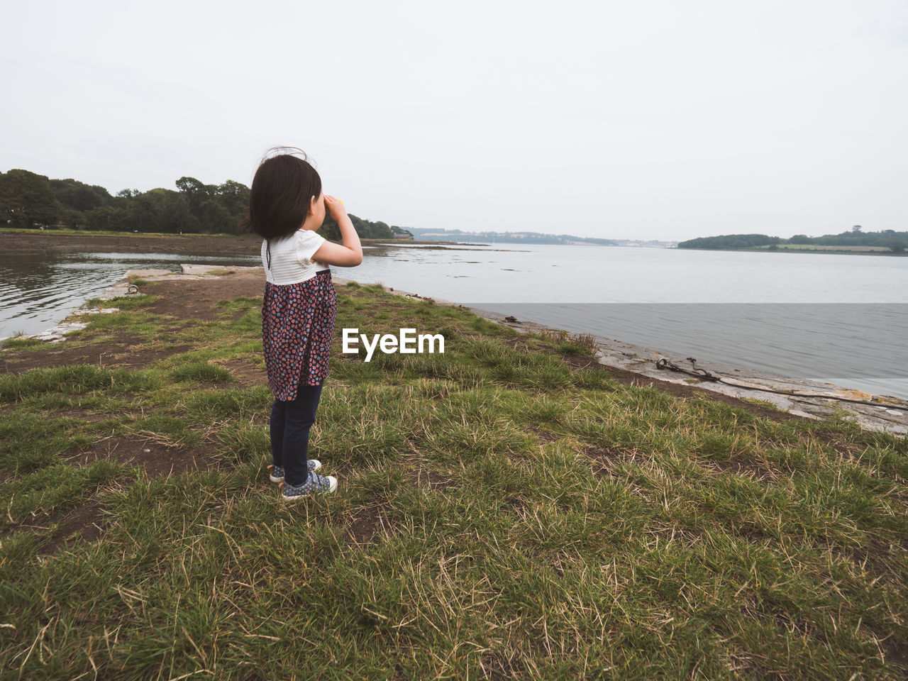 Girl standing on lakeshore against sky