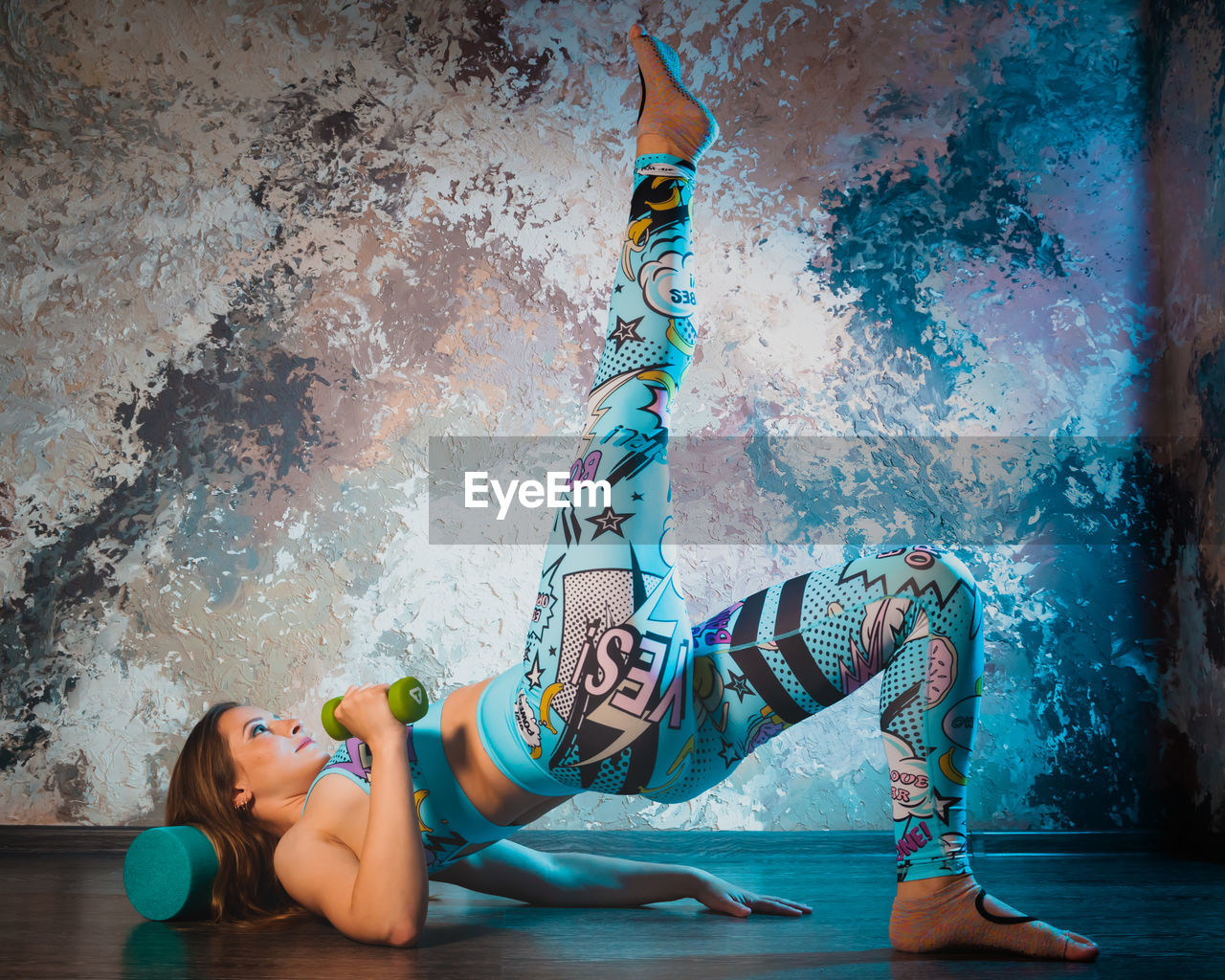 A young athletic girl in bright sportswear is doing fitness on the floor in a studio or gym