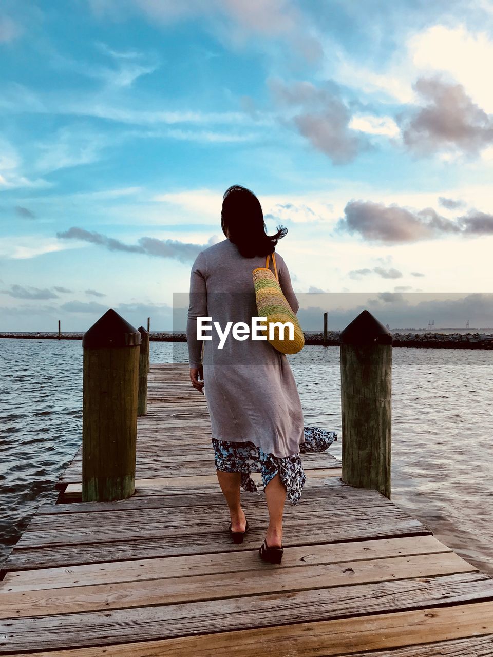 Rear view of woman walking on pier over lake against sky