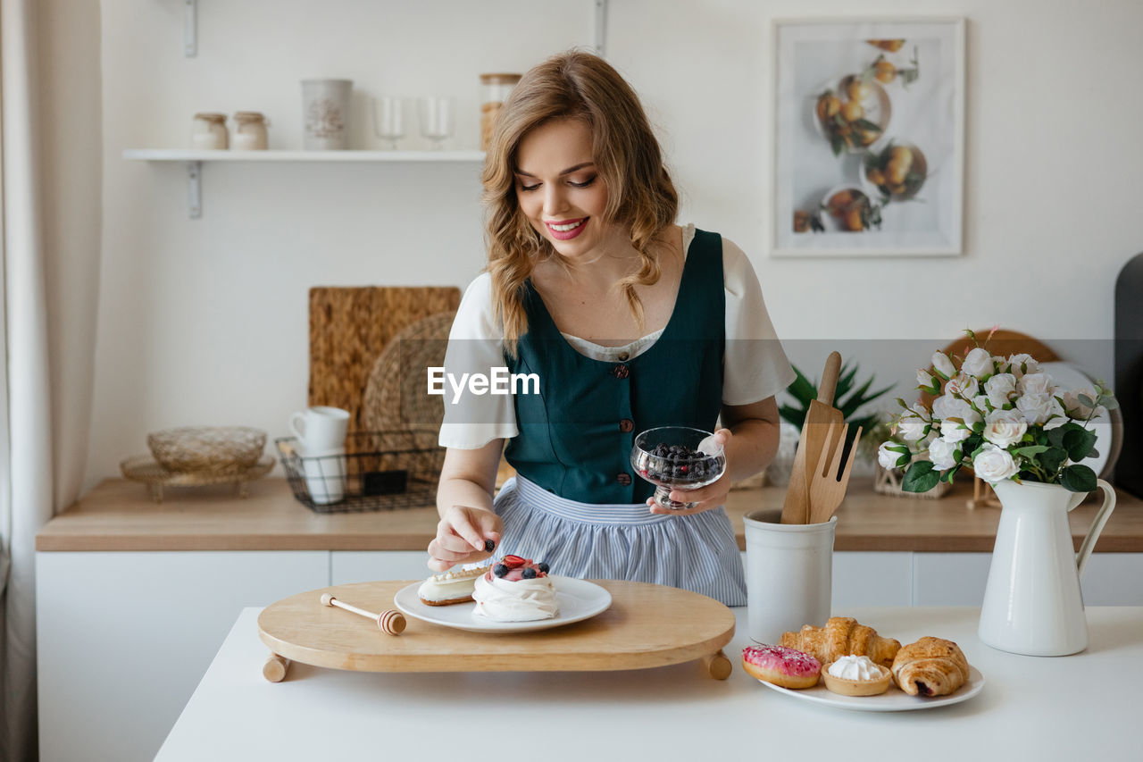 Beautiful girl adds a berry to the cake in the kitchen