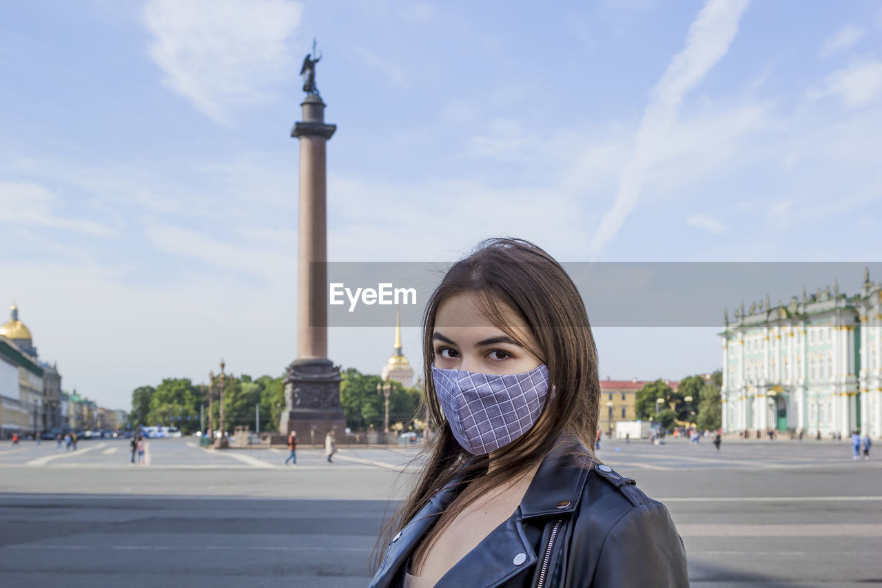 Portrait beautiful young woman in medical mask on palace square in st. petersburg. positive fashion