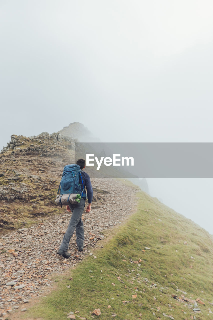 Back view of faceless male hiker walking along trail in highlands during trekking on foggy day in wales