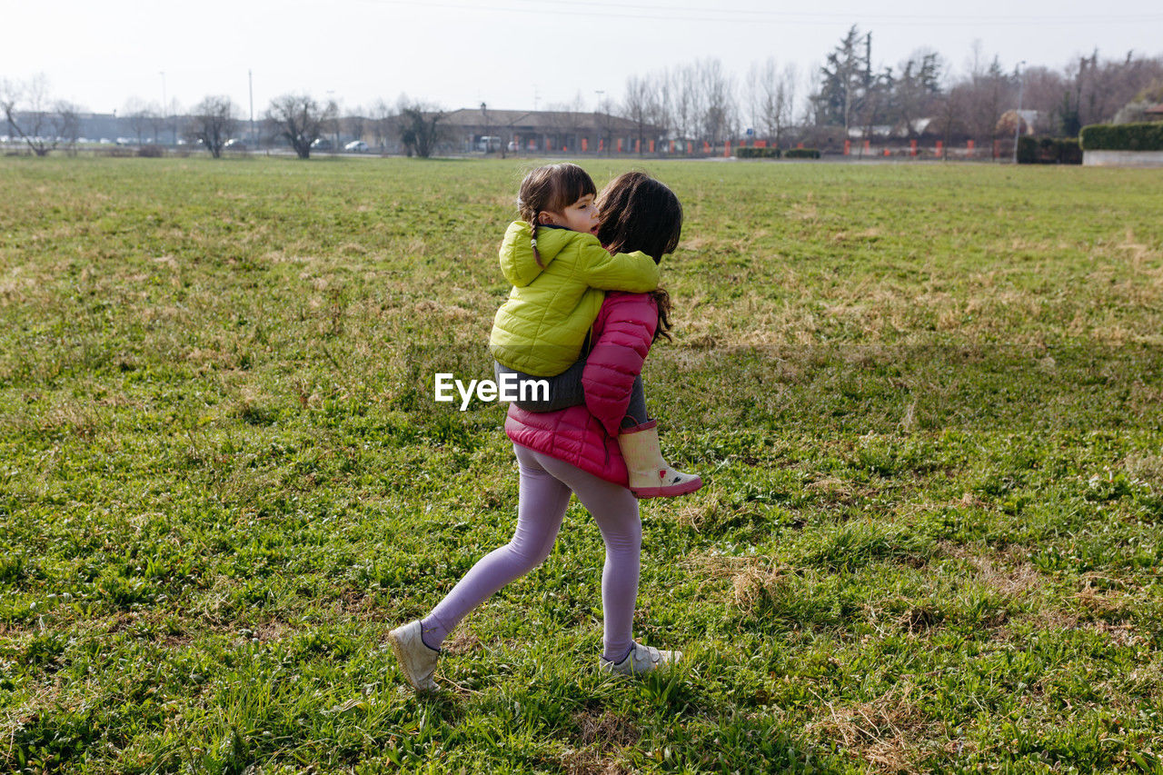 Small child riding piggyback on elder sister outdoors in the field