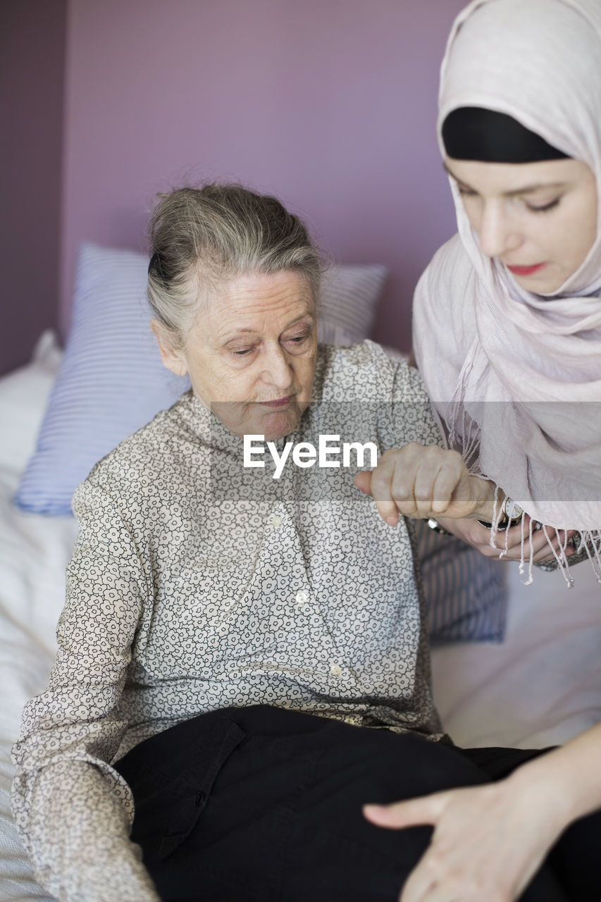 Senior woman being assisted by female home caregiver in bed