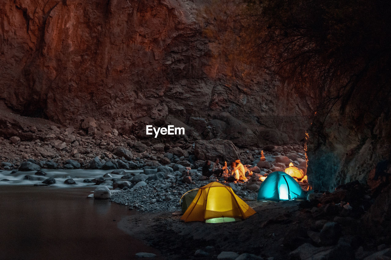 Illuminated tents by rock formations at night