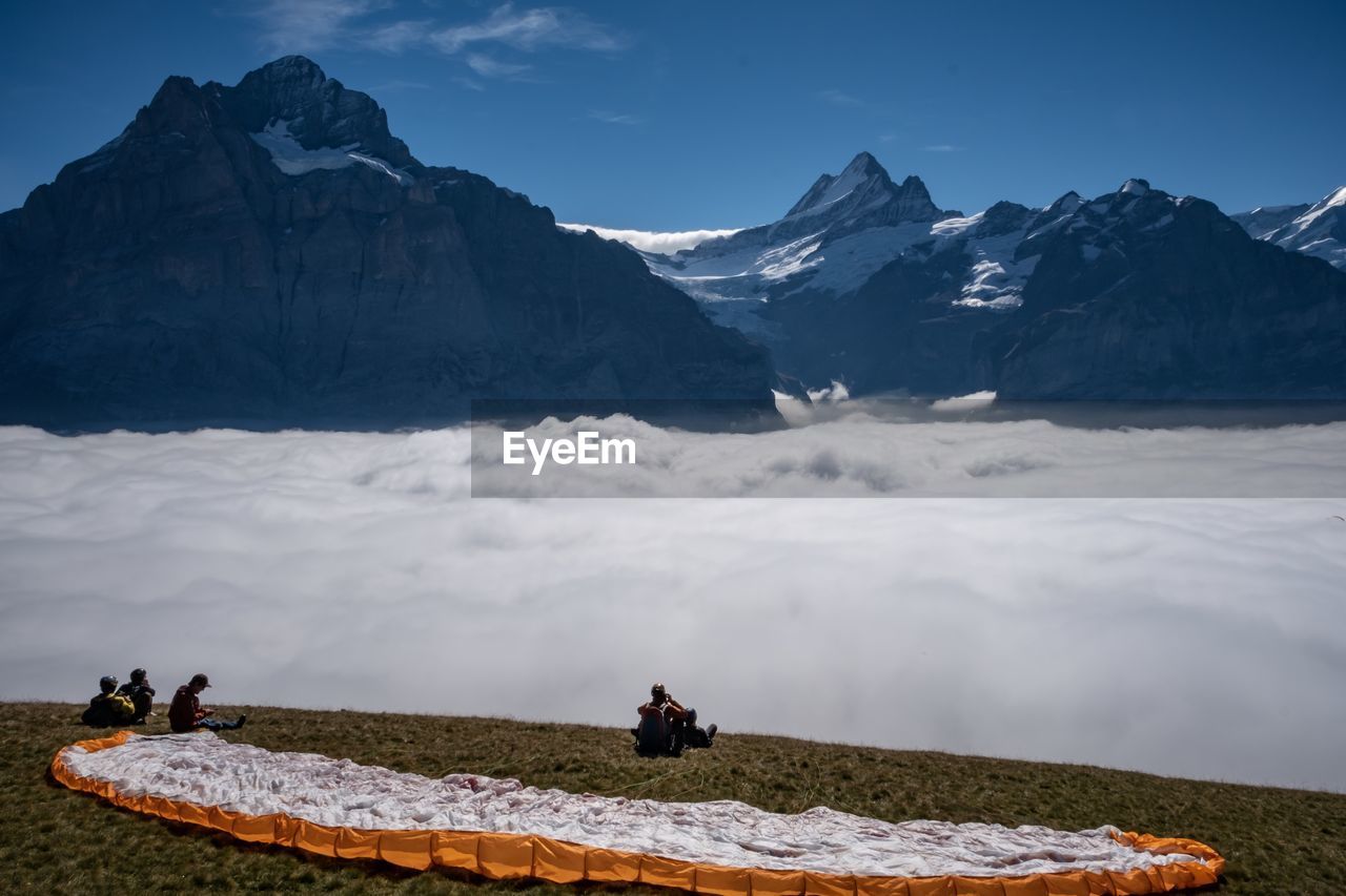 People sitting on field by cloudscape against mountains