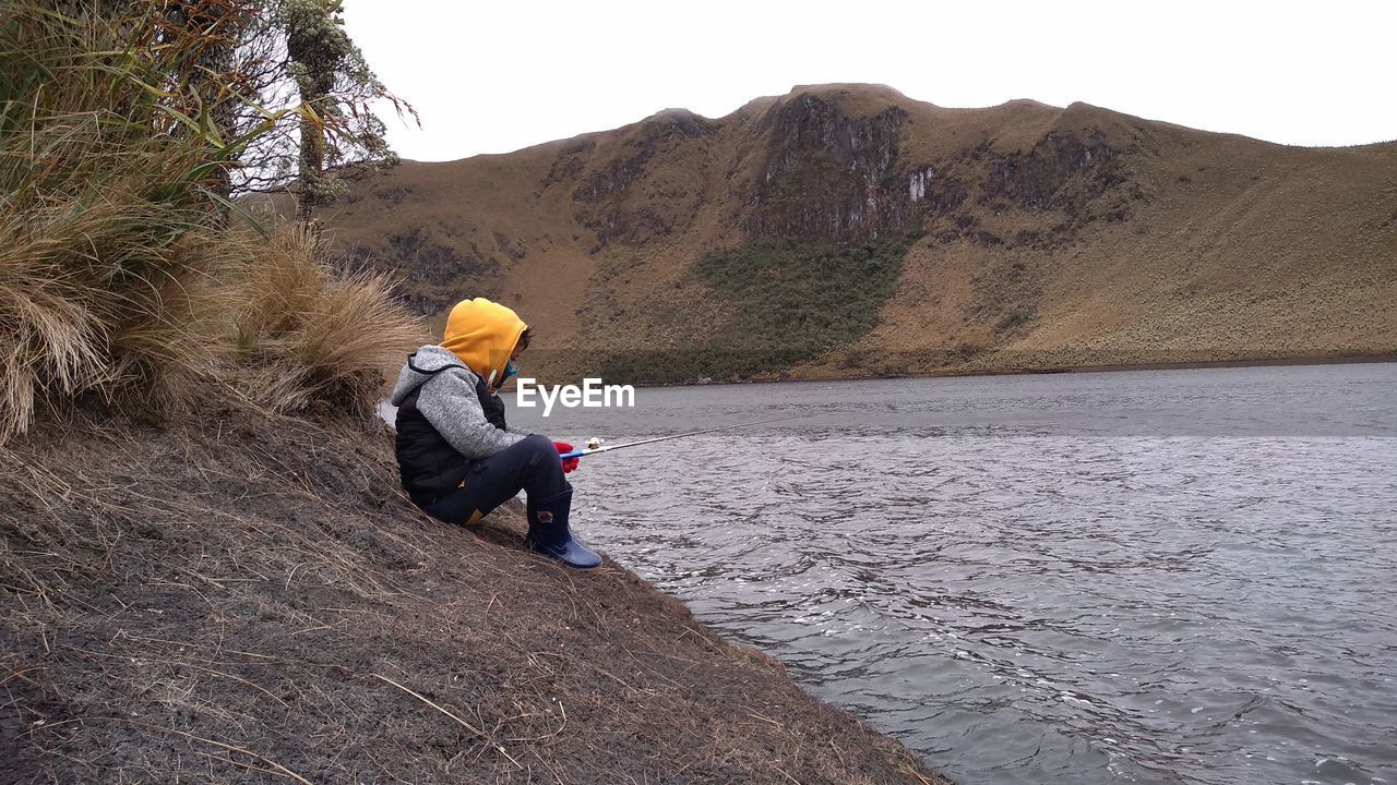 Side view of boy fishing in on lake by mountain