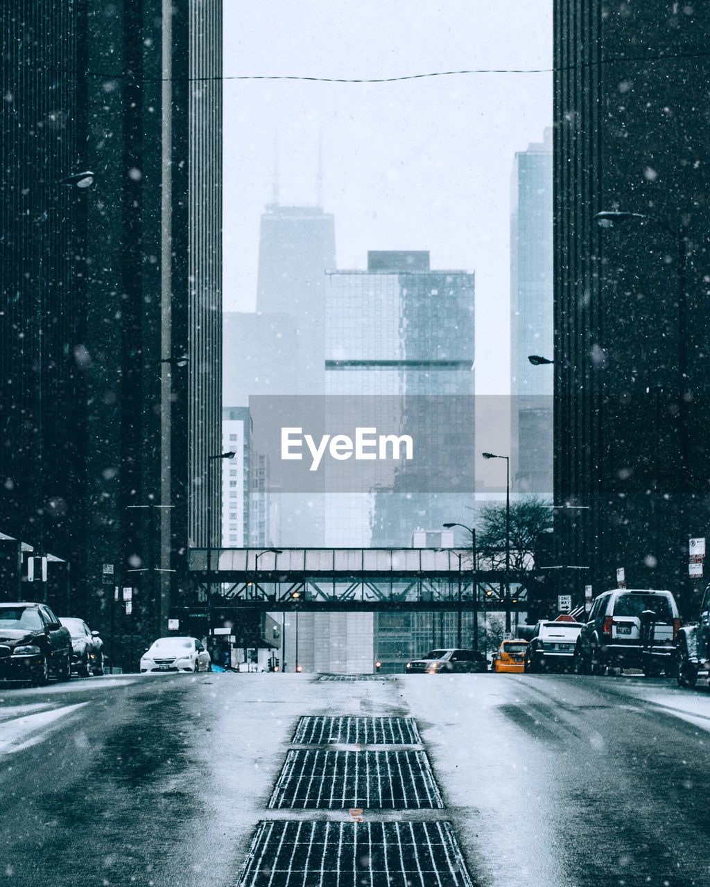 Road amidst buildings in city during snowfall