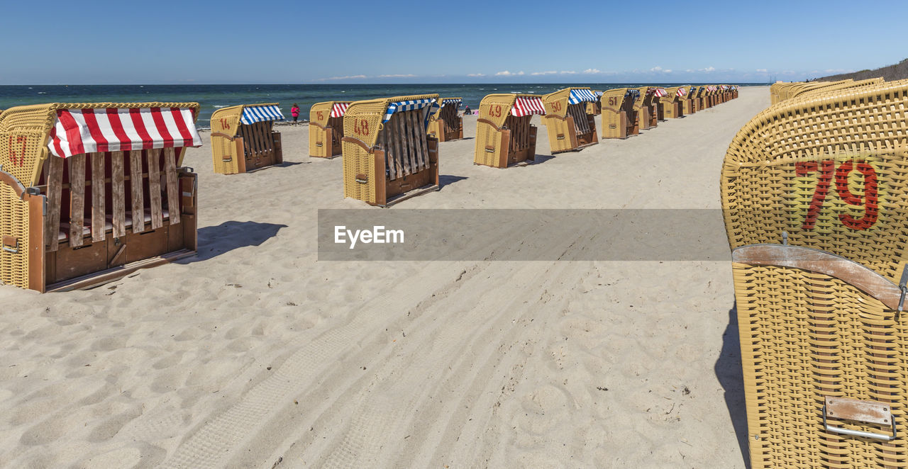 HOODED BEACH CHAIRS ON SAND AT SHORE AGAINST SKY