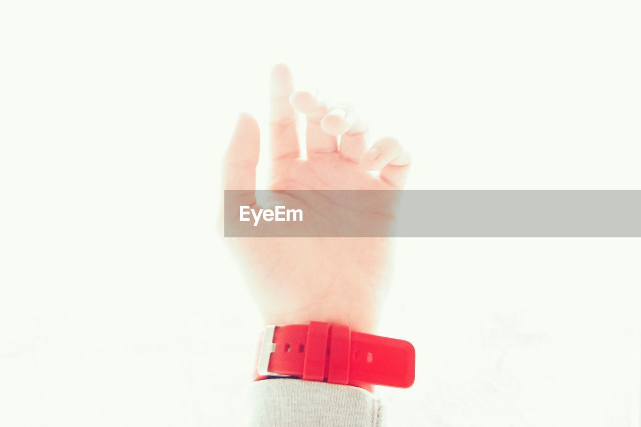 Cropped image of hand wearing red wristwatch against white background