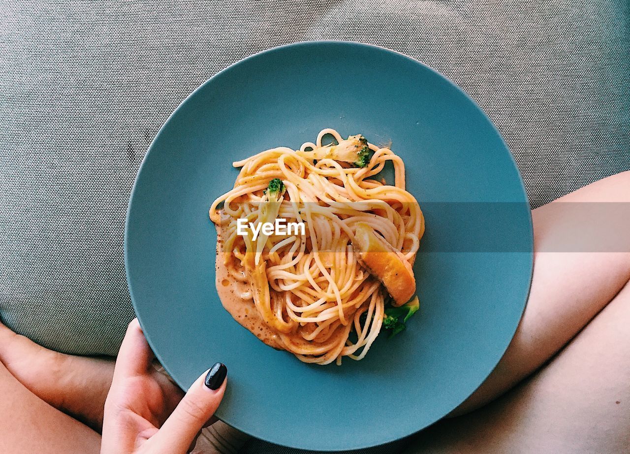 Low section of woman holding pasta in plate on bed 