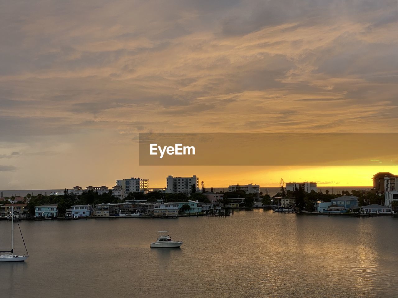 SEA BY BUILDINGS AGAINST SKY AT SUNSET