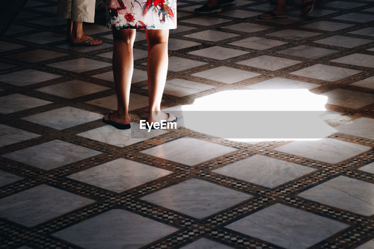 flooring, low section, human leg, women, floor, one person, adult, pattern, standing, tiled floor, shoe, black, tile, indoors, human limb, lifestyles, day, limb, clothing, architecture, red, walking, dress, fashion, casual clothing, sunlight, leisure activity