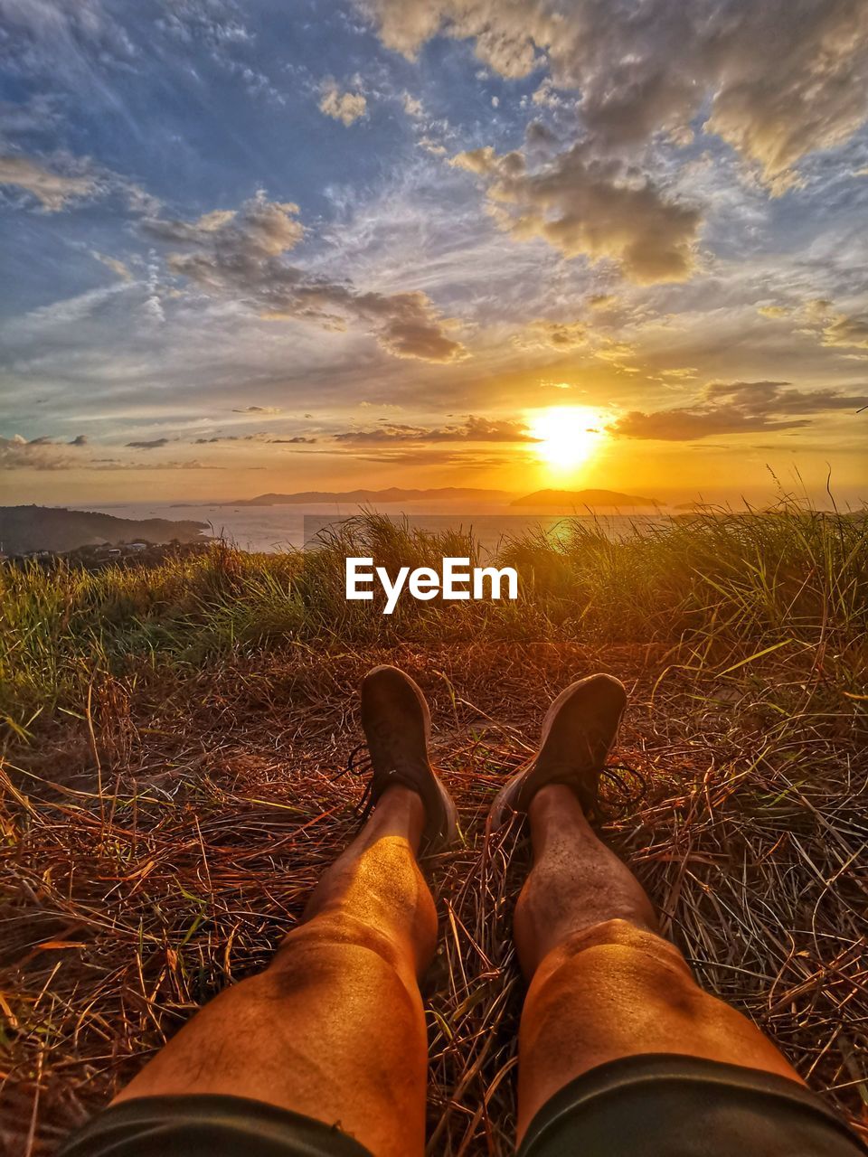 Low section of person on field against sky during sunset