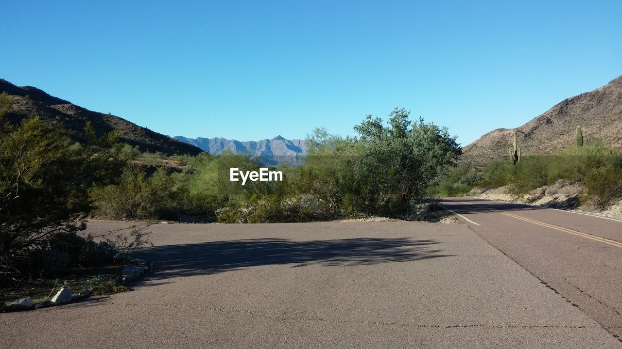 Road leading towards mountains against clear blue sky