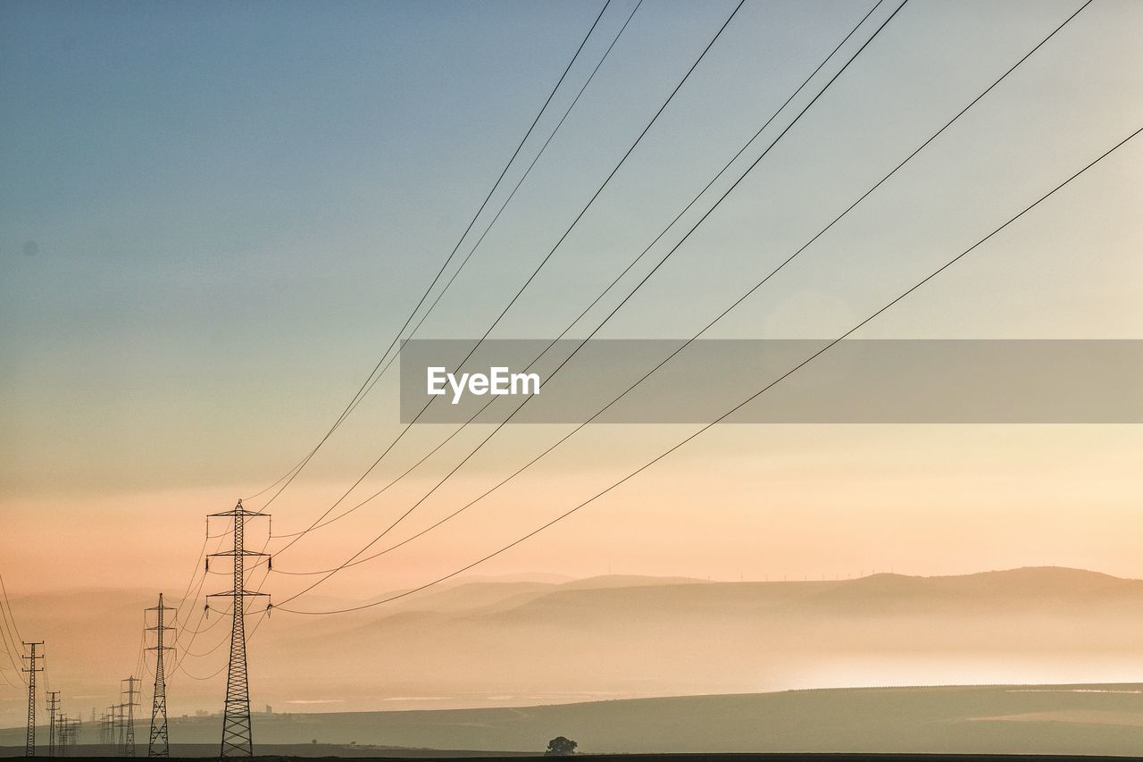Low angle view of electricity pylons against sky during sunset