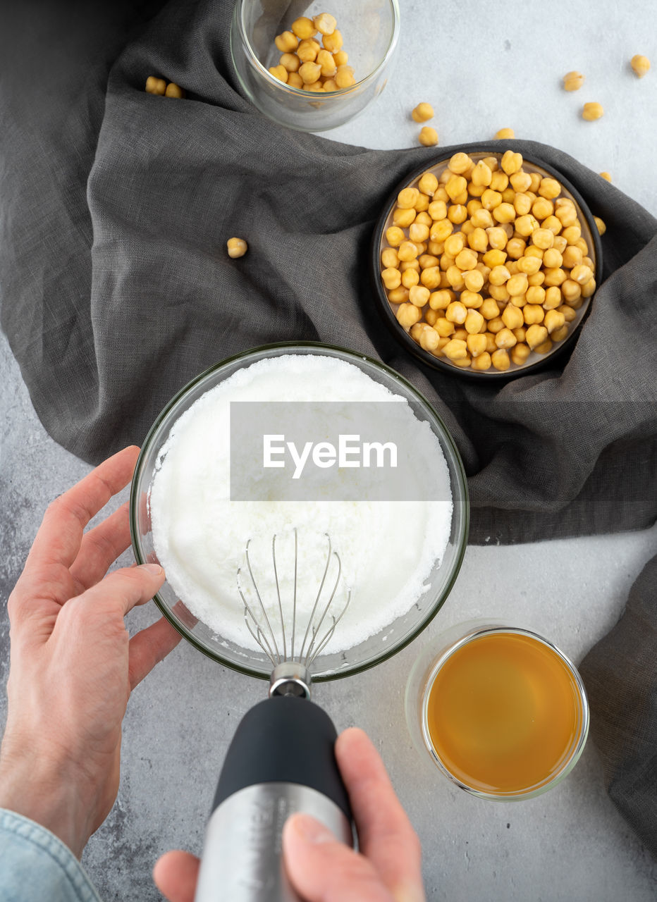 Chickpea aquafaba. egg replacement. vegan. men hands whippe whisk chickpeas liquid in glass bowl