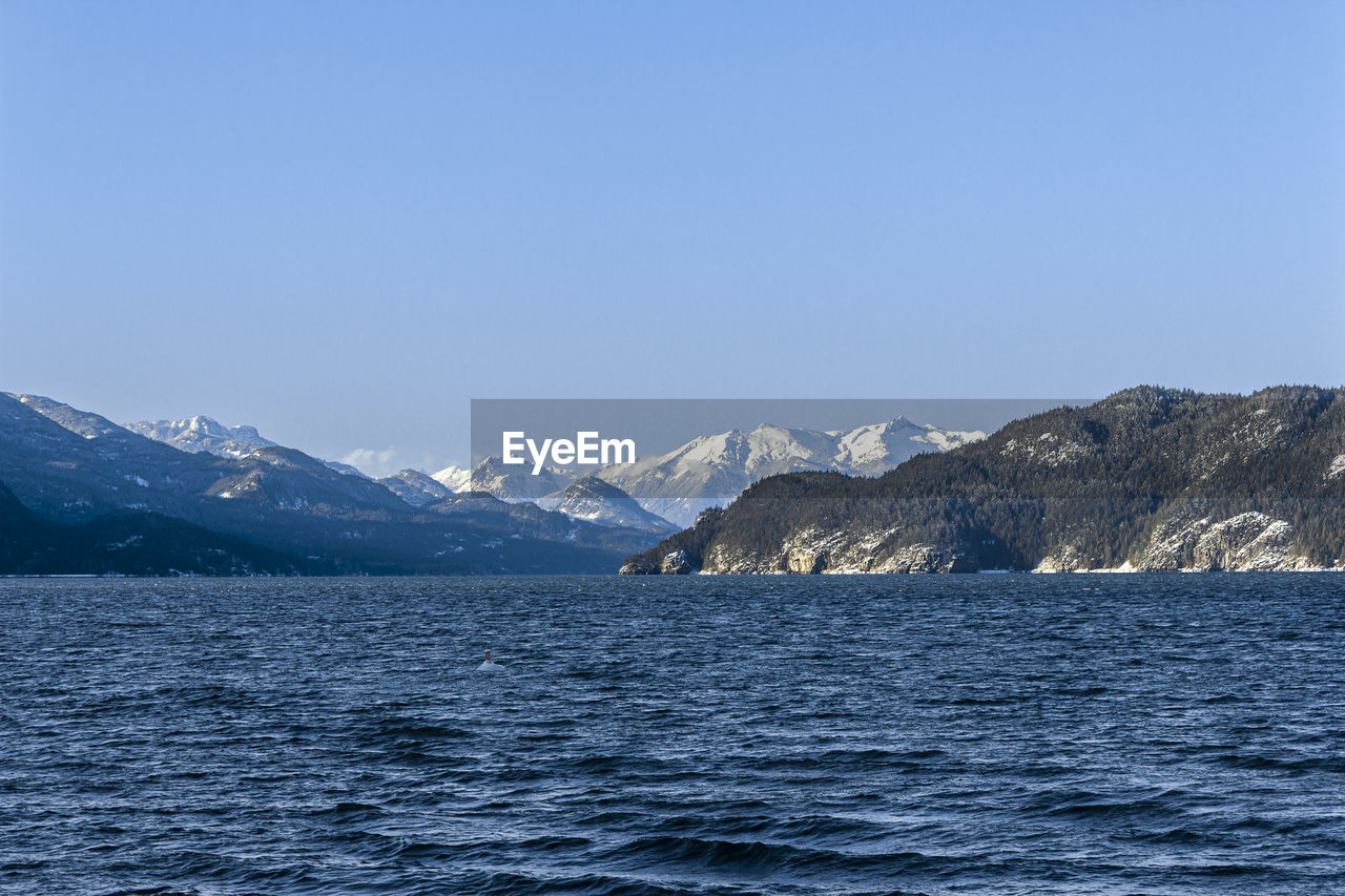 Scenic view of sea and snowcapped mountains against clear blue sky