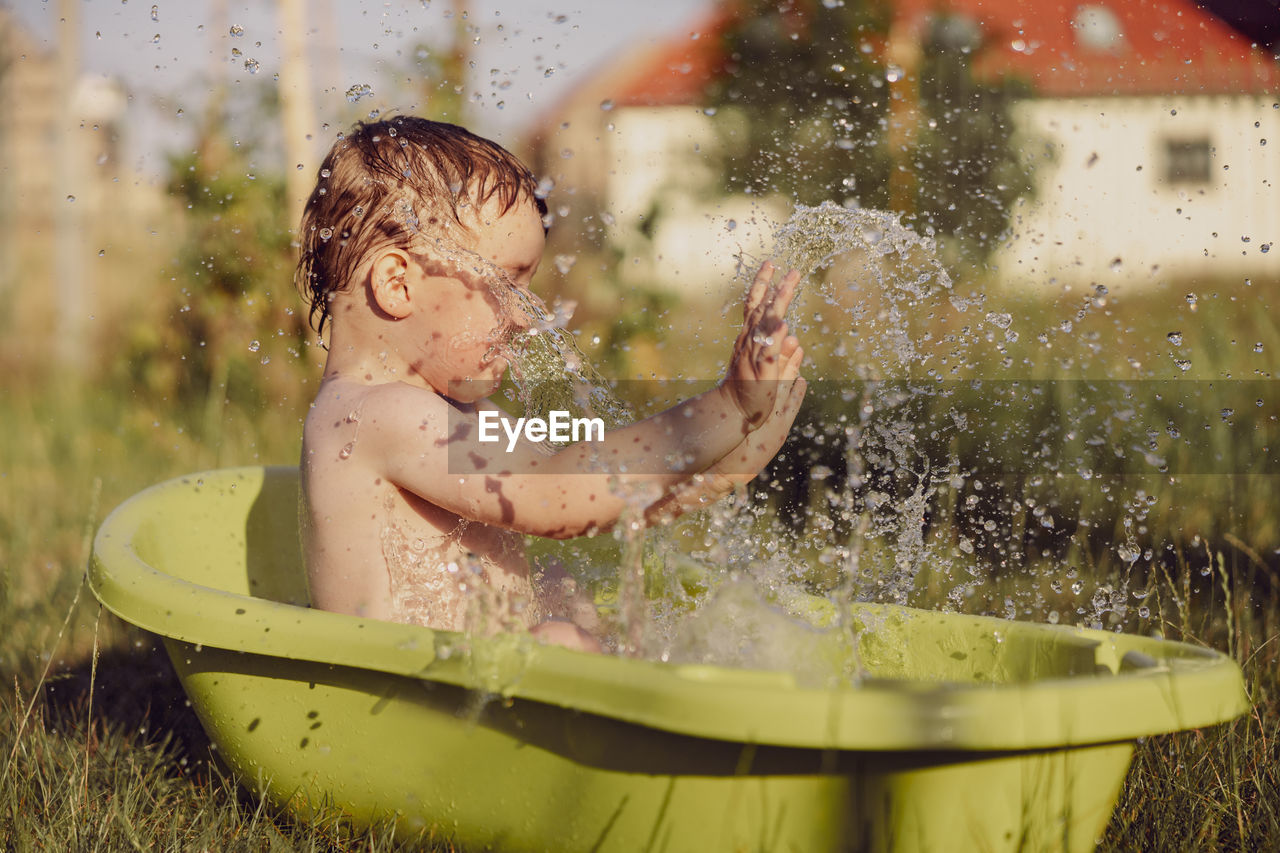 Cute little boy bathing in tub outdoors in garden. happy child is splashing, playing with water 