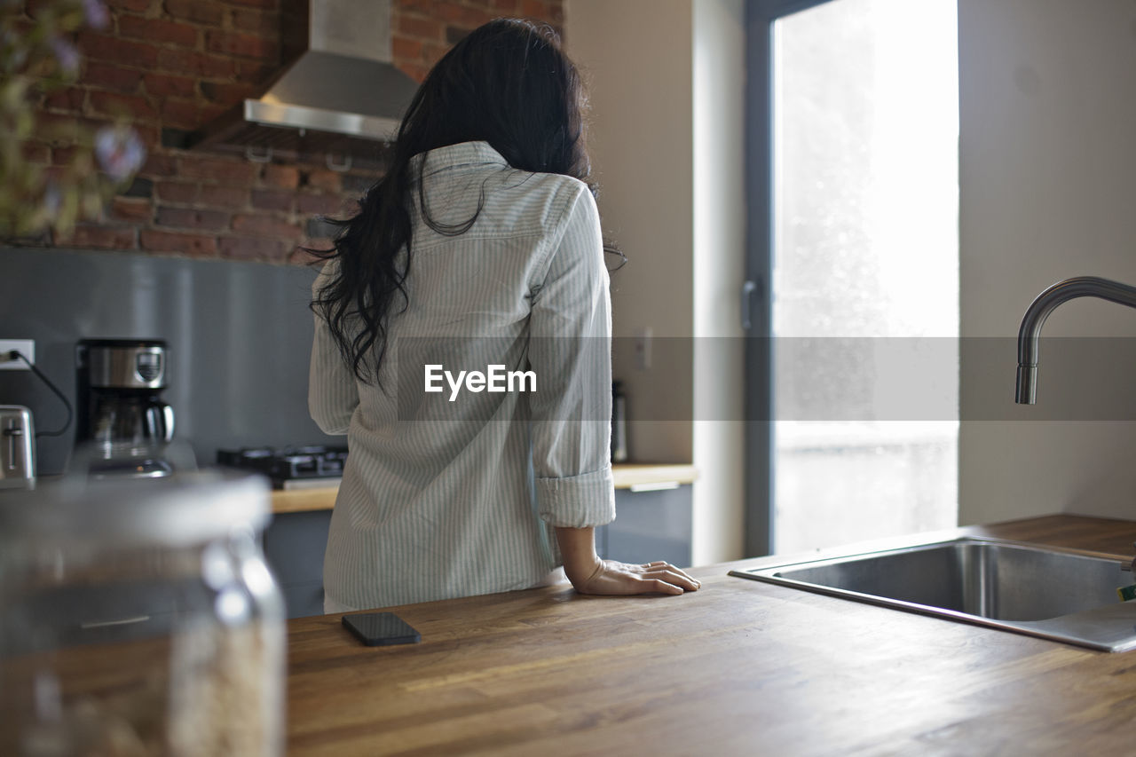 Rear view of woman standing in kitchen at home