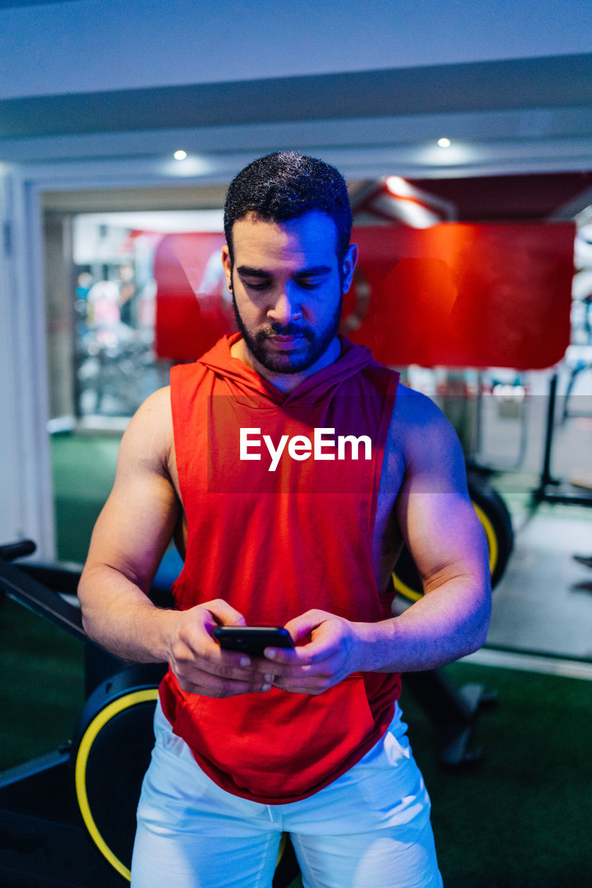 Portrait of young man typing on mobile phone checking exercises at gym