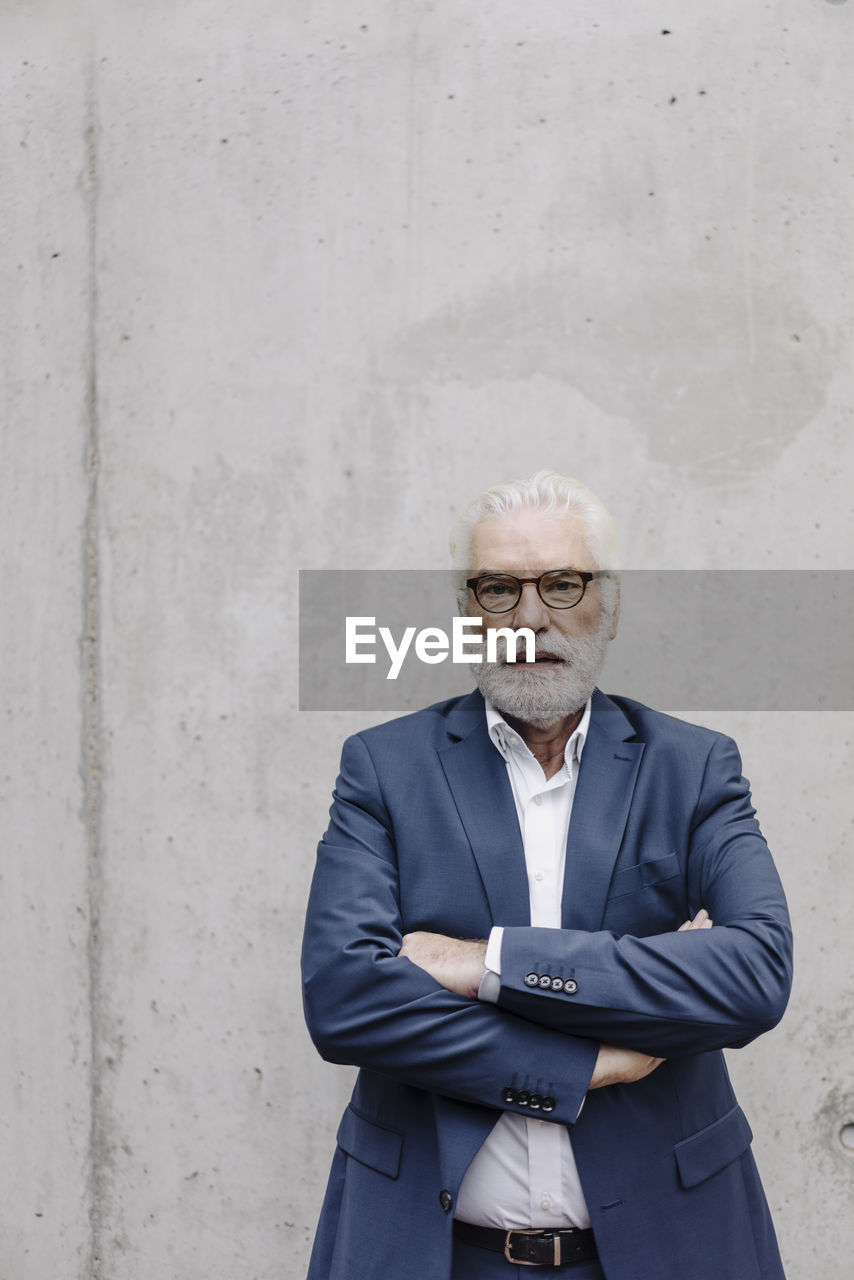 Portrait of serious senior businessman standing at a concrete wall