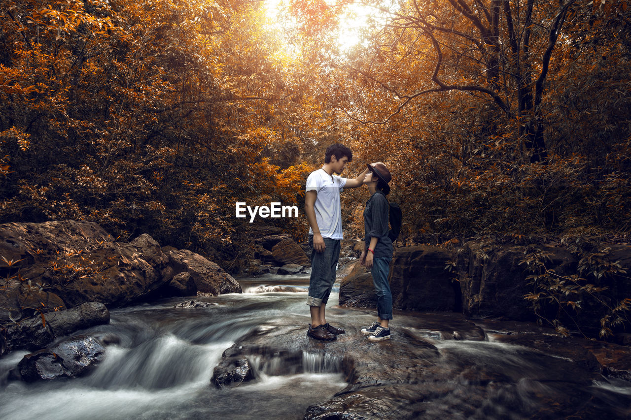 Young couple standing at river in forest during autumn