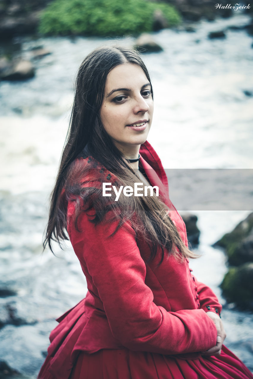 PORTRAIT OF SMILING YOUNG WOMAN STANDING ON RIVER