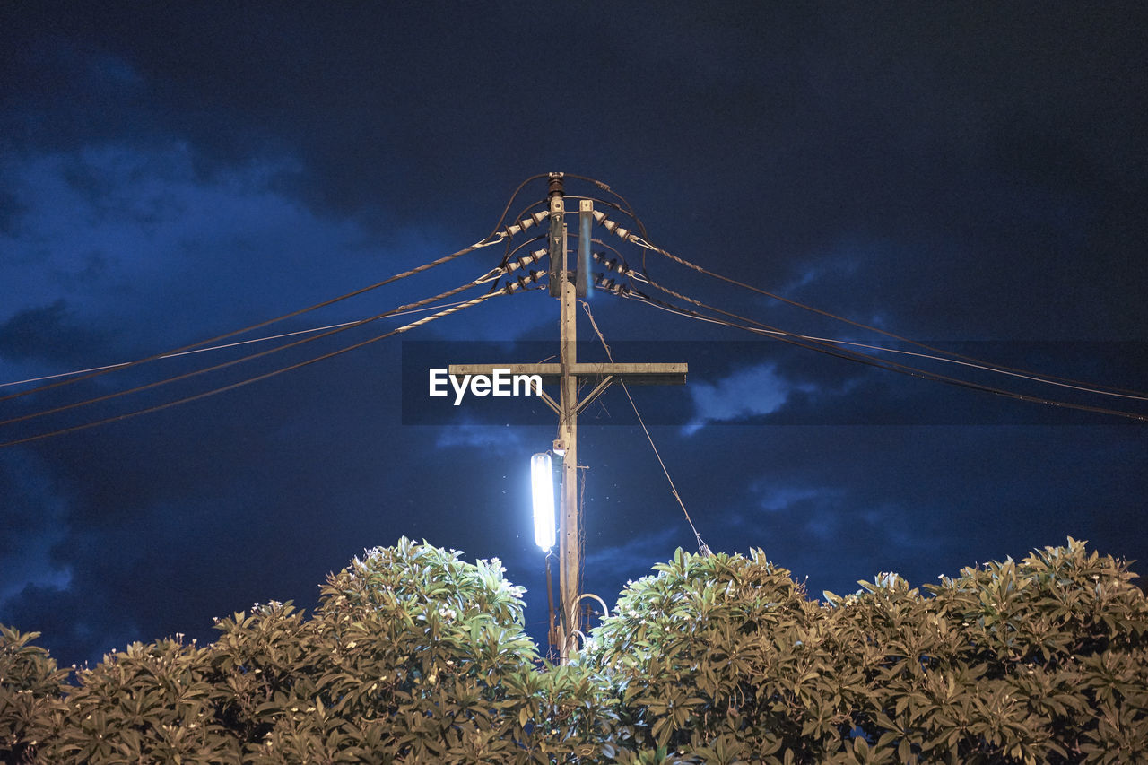Low angle view of power line against cloudy sky at night