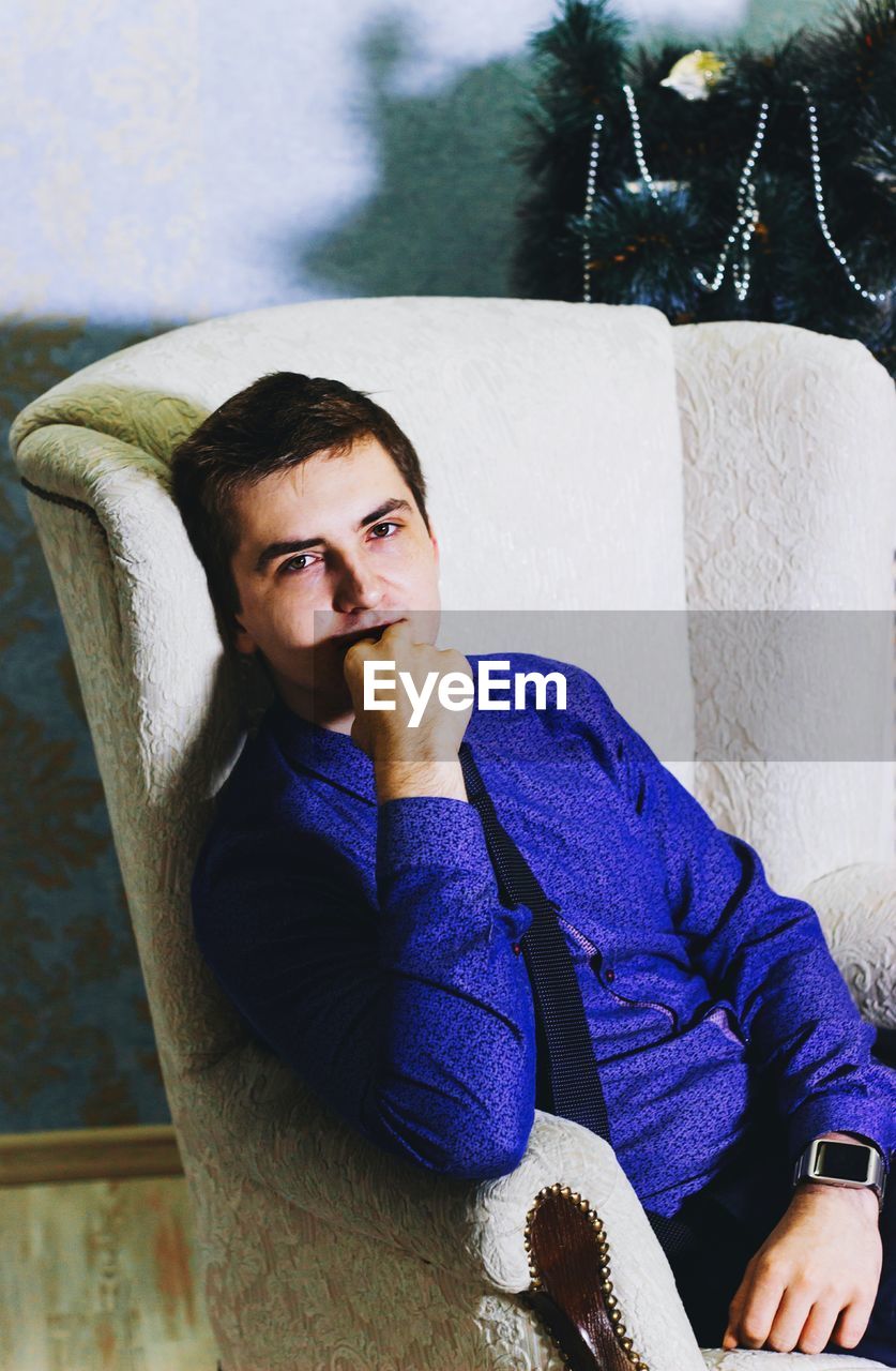 Portrait of man wearing purple shirt relaxing on armchair at home during christmas