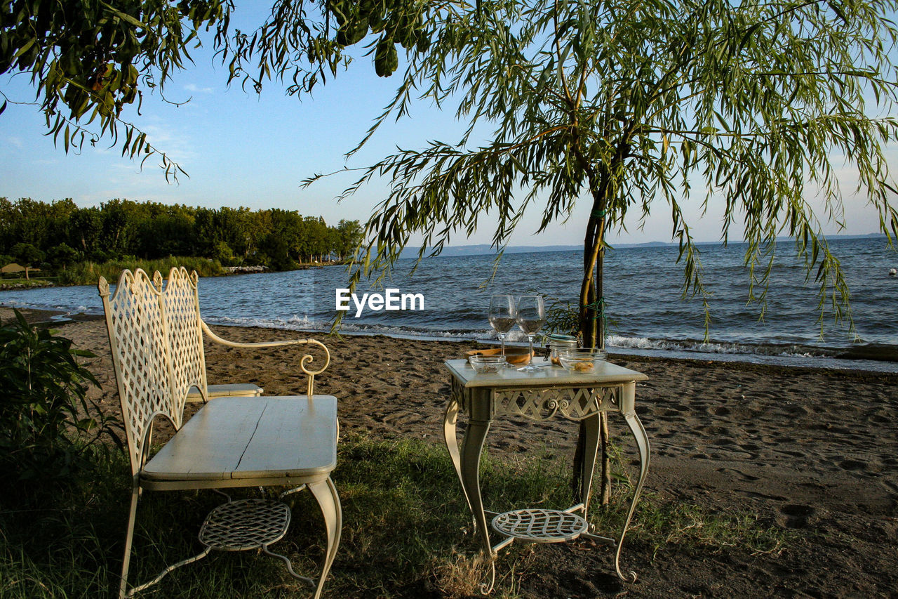 Empty chairs and table at beach against sky