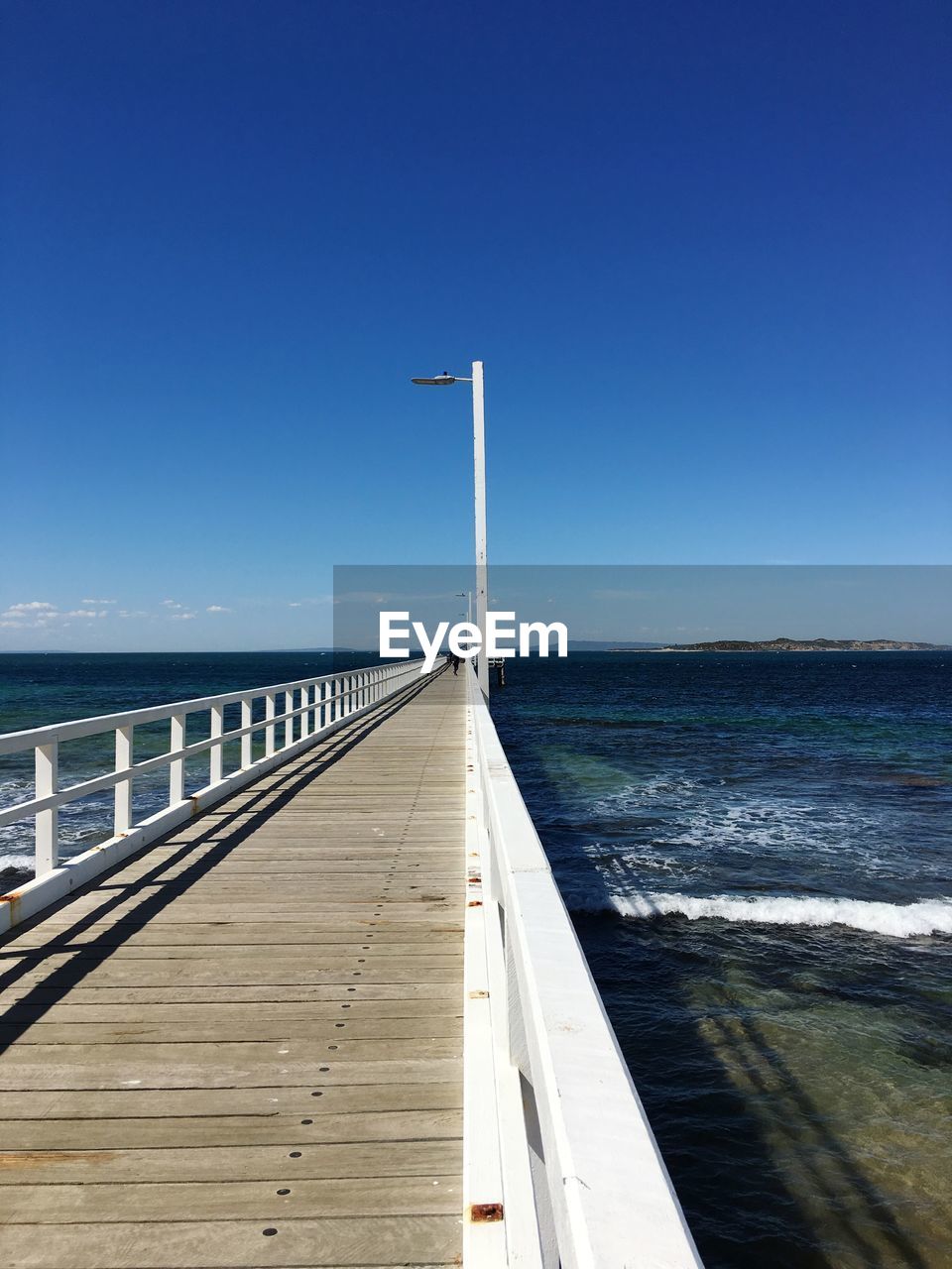 Pier on sea against clear blue sky