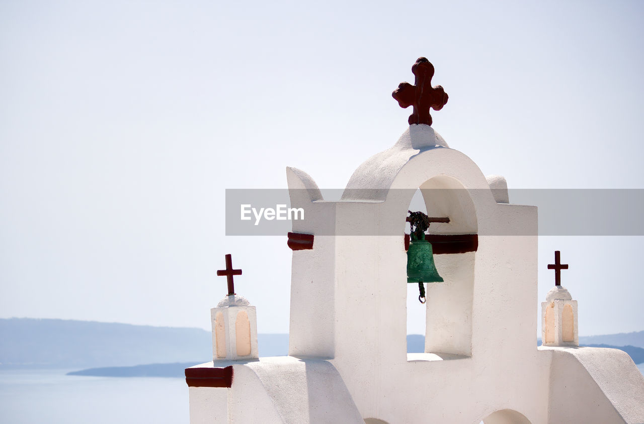 Top of a church with cross sign and bells architecture in one of cycladic island in santorini