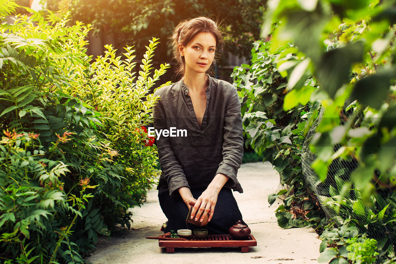 PORTRAIT OF BEAUTIFUL YOUNG WOMAN WITH PLANTS IN FOREGROUND