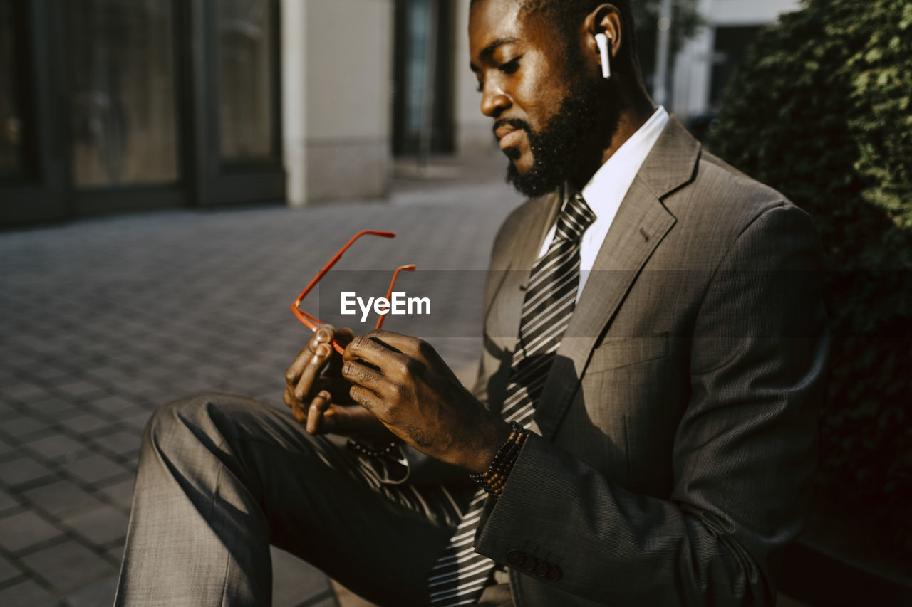 Male entrepreneur looking at eyeglasses while sitting on footpath