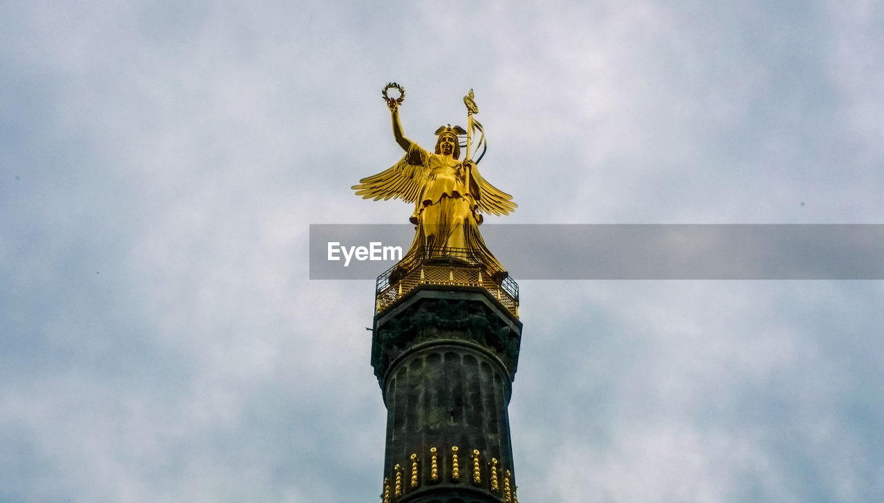 Low angle view of victory statue in berlin against cloudy sky