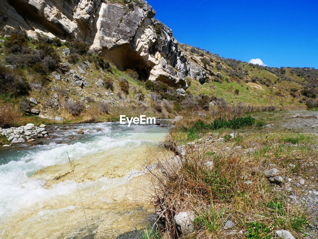 SCENIC VIEW OF WATER FLOWING THROUGH ROCKS AGAINST SKY