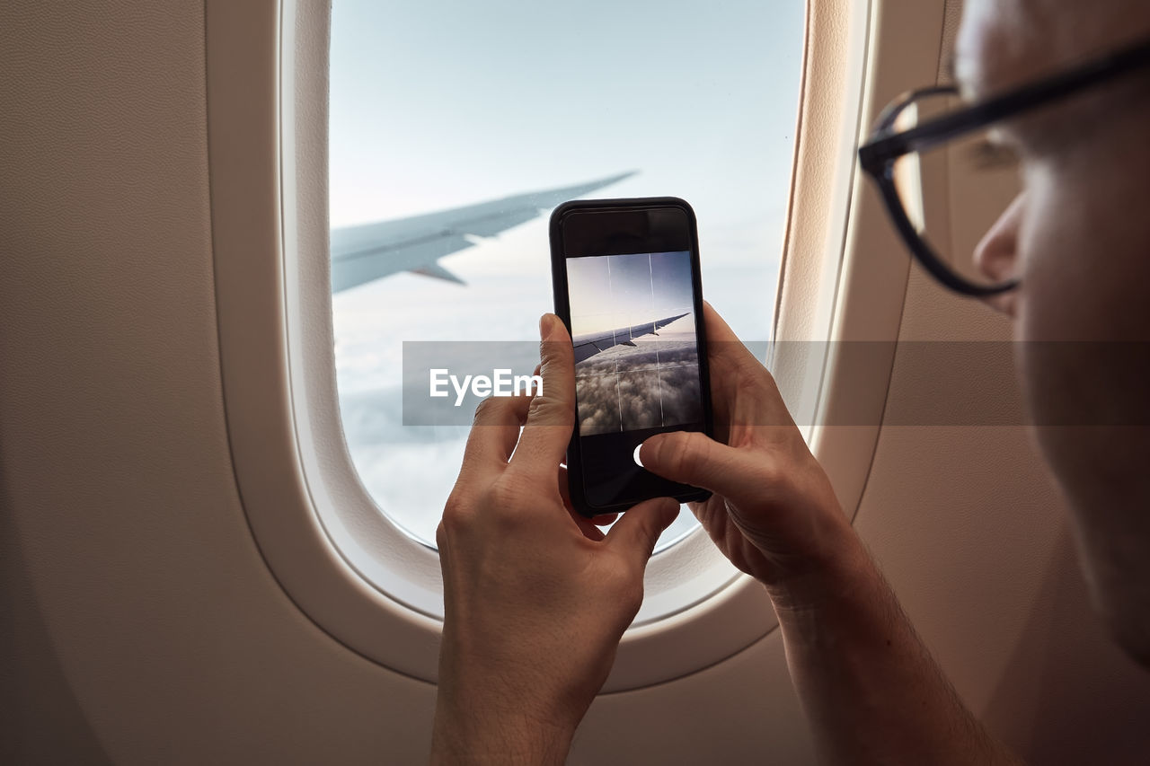 Cropped image of person photographing through airplane window