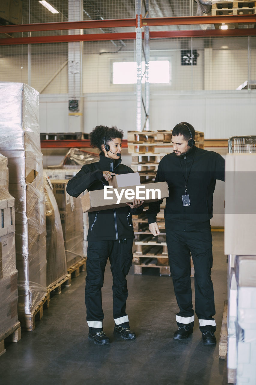 Female entrepreneur holding packages while discussing with male colleague in logistics warehouse